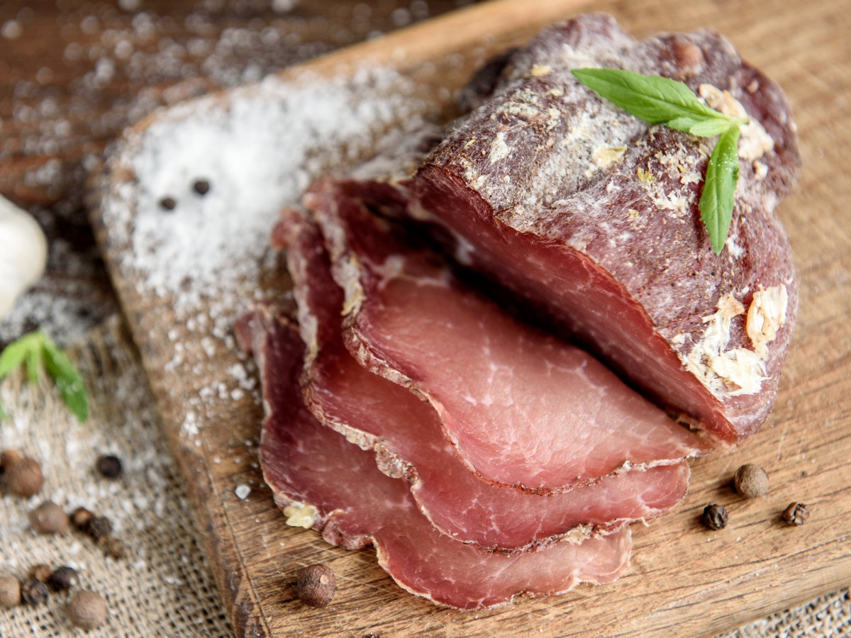 Pork dried meat slices on rustic dark wooden background. Dried pork prosciutto salami ham with herbs.