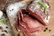 Pork dried meat slices on rustic dark wooden background. Dried pork prosciutto salami ham with herbs.