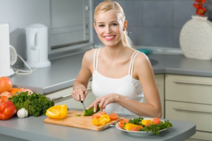 Young happy woman making salad at domestic kitchen