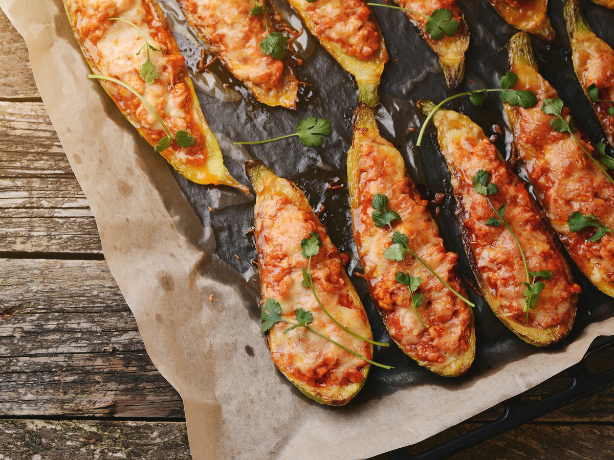 Baked stuffed zucchini with meat in a pan on wooden boards.