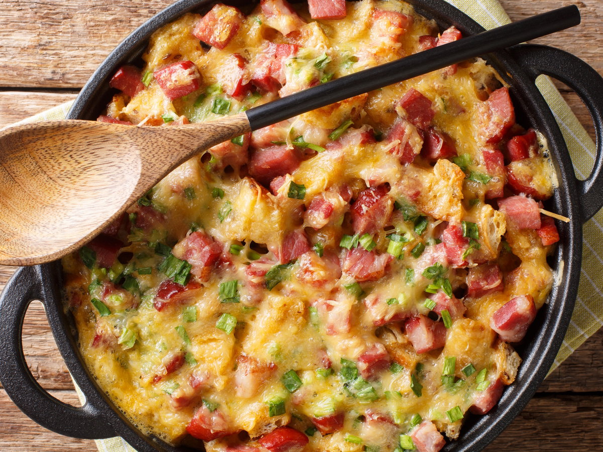 recipe for a simple strata with ham, bread, onions, cheese and eggs close-up in a pan. Horizontal top view