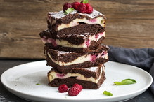 Brownies-cheesecake tower with raspberries on white plate, wooden backdrop, copy space