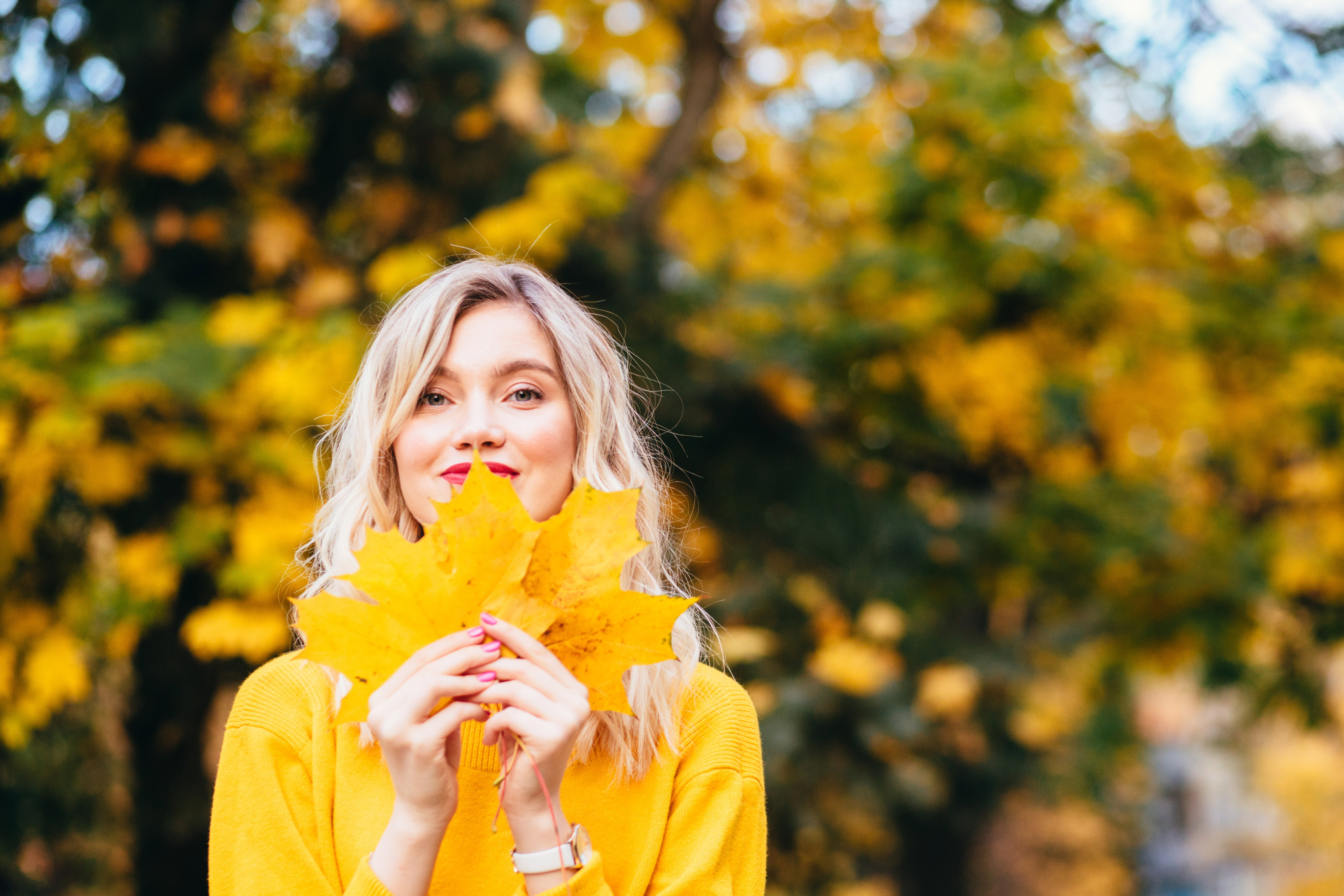 Autumn walk. Woman portrait. Happy girl in yellow hoodie and jean jacket is playing with leaf, looking at camera and smiling while lying on the ground in the park top view