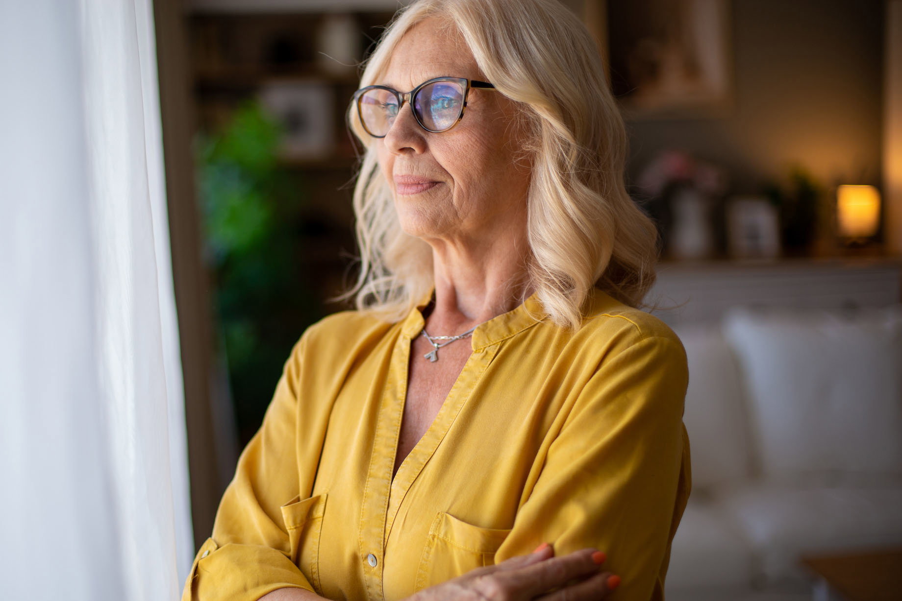 Senior woman looking through window while contemplating life at home