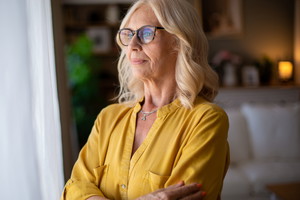 Senior woman looking through window while contemplating life at home