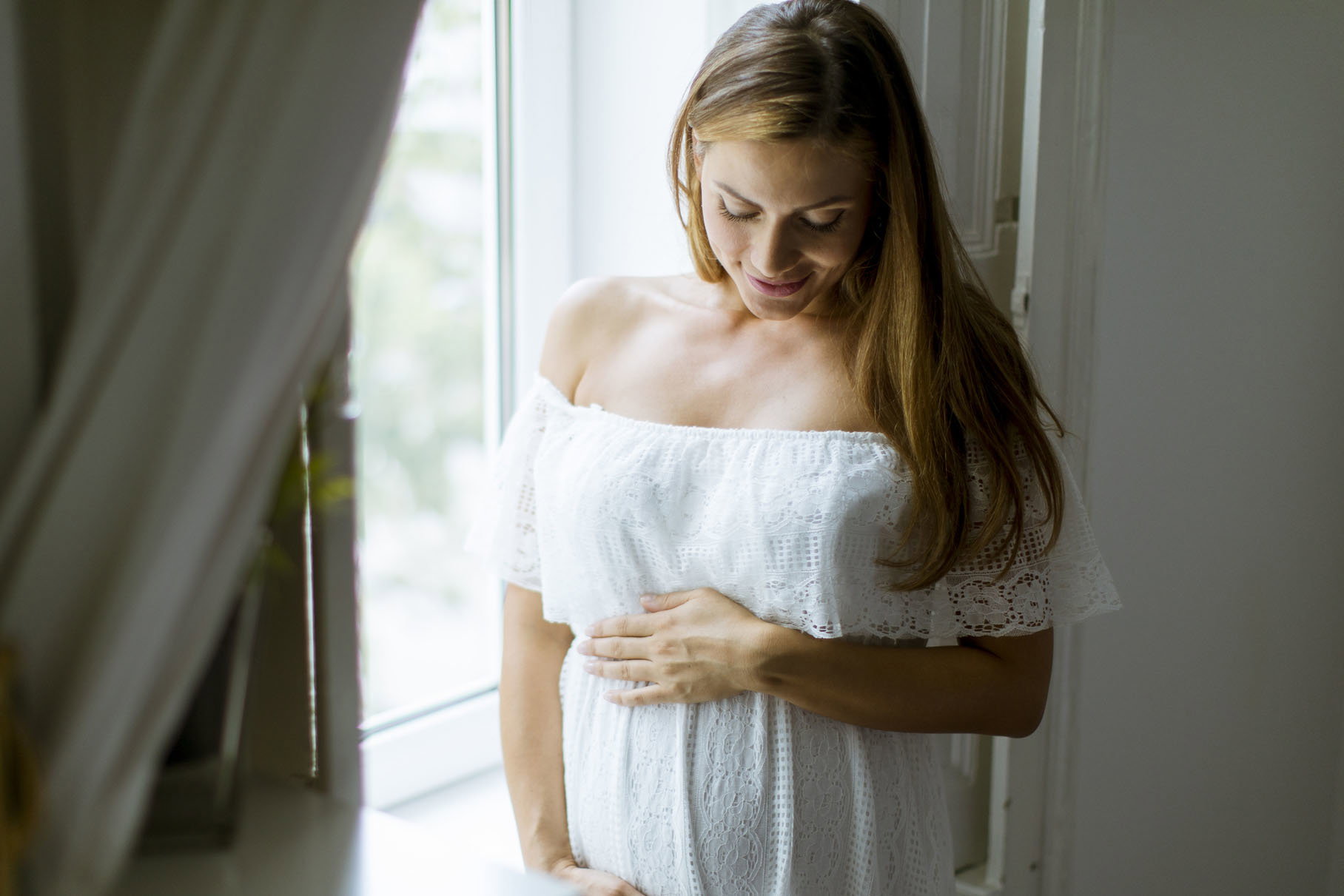 Young pregnant woman standing by the window