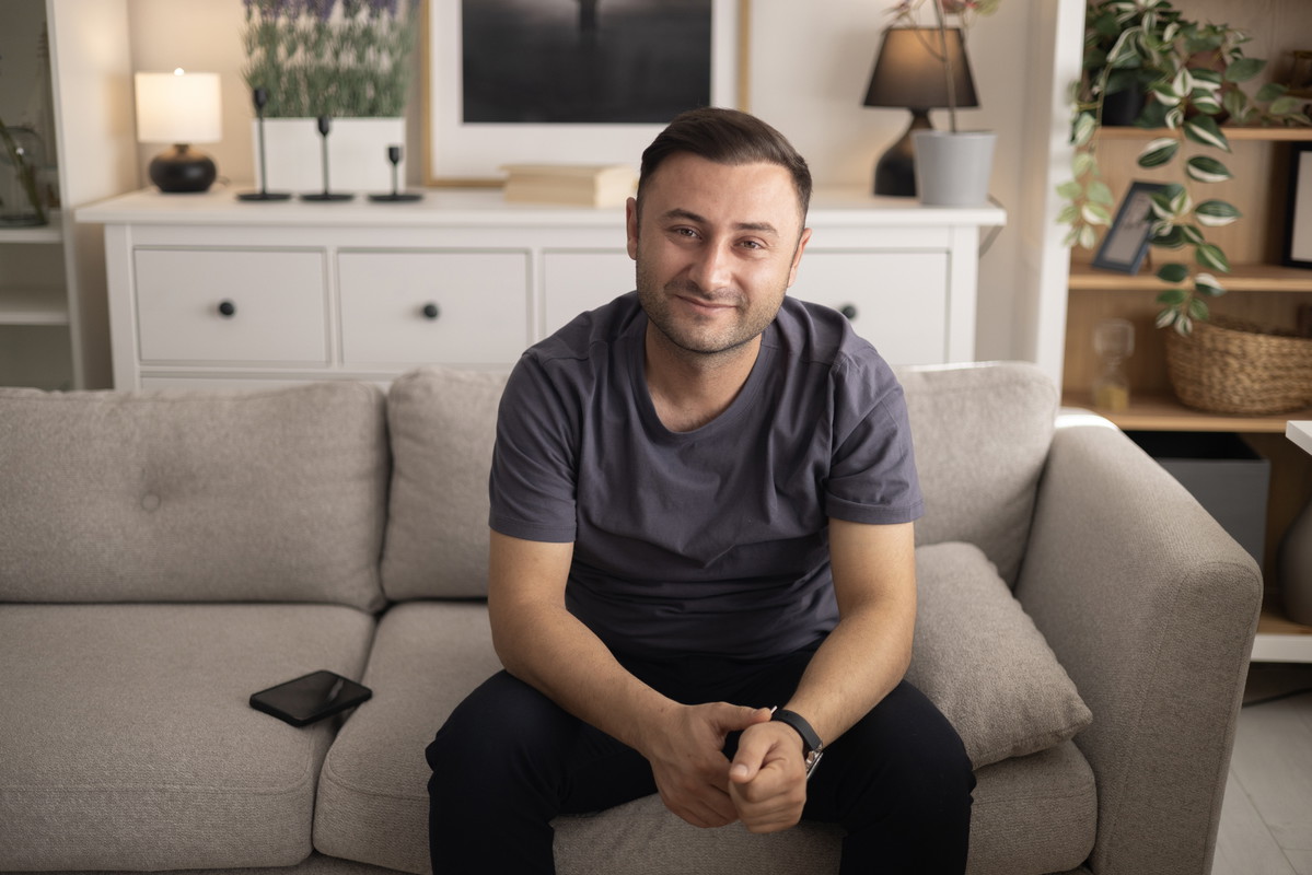 Adult man enjoying free time, sitting on a comfortable sofa in his modern living room, looking at camera