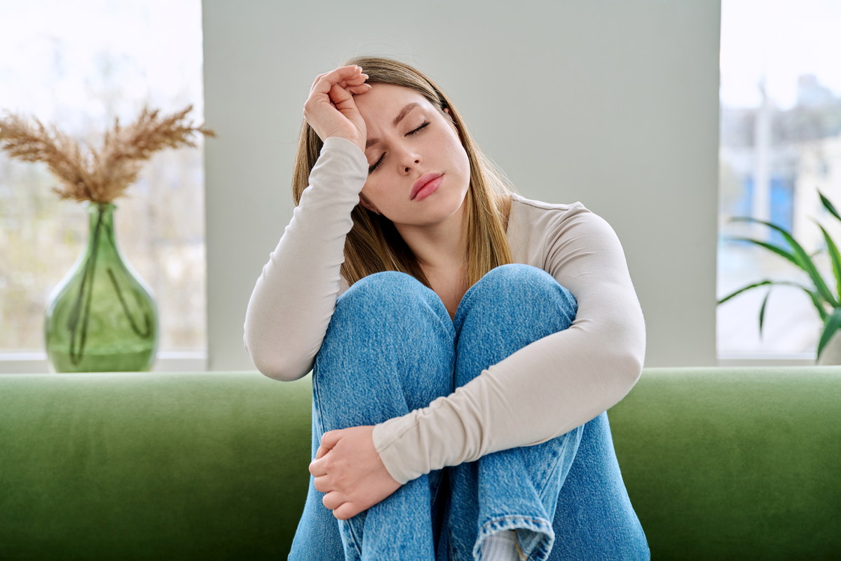 Unhappy upset young woman sitting on sofa at home, face close-up