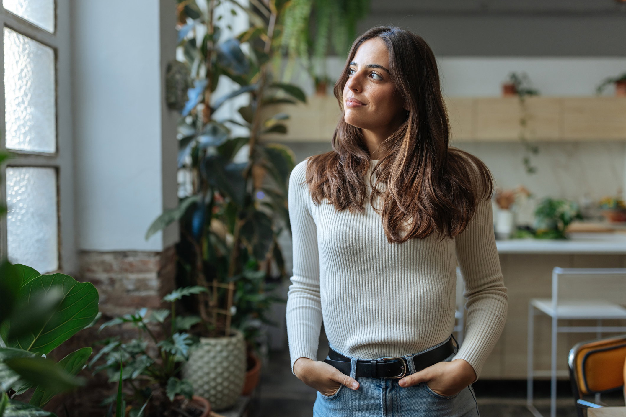 Young woman looking out the window in a plant-filled room