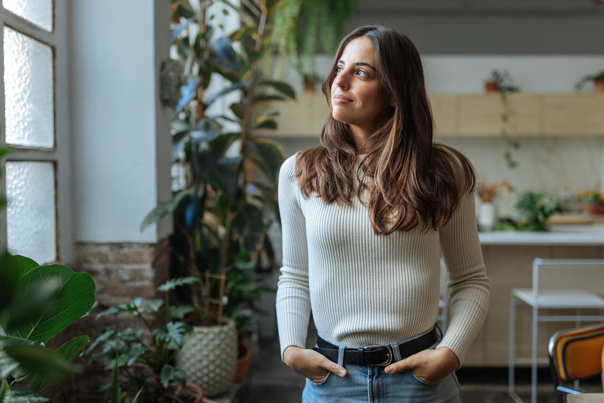 Young woman looking out the window in a plant-filled room