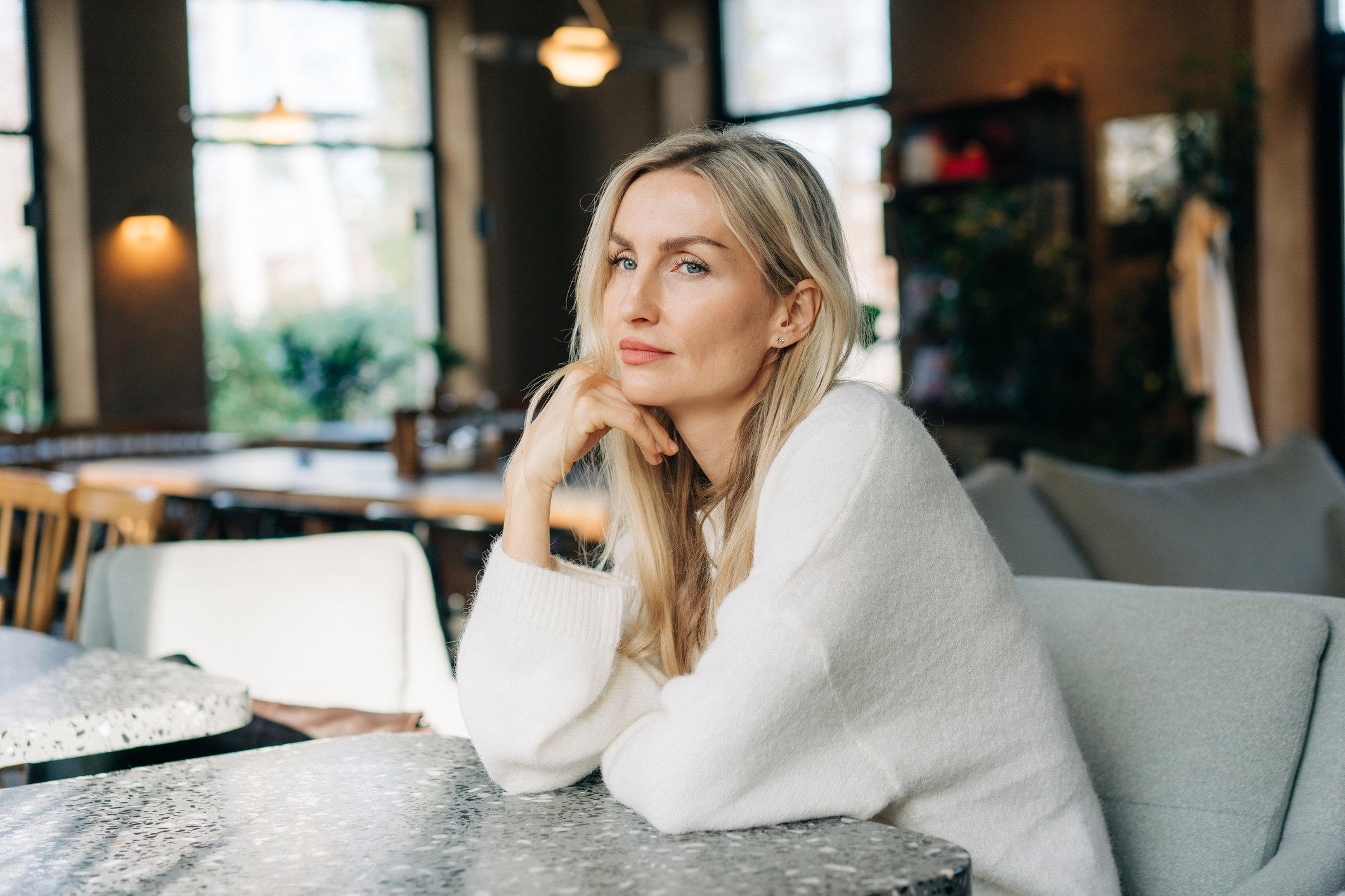 Beautiful pensive blonde woman with long hair sitting in a cafe.