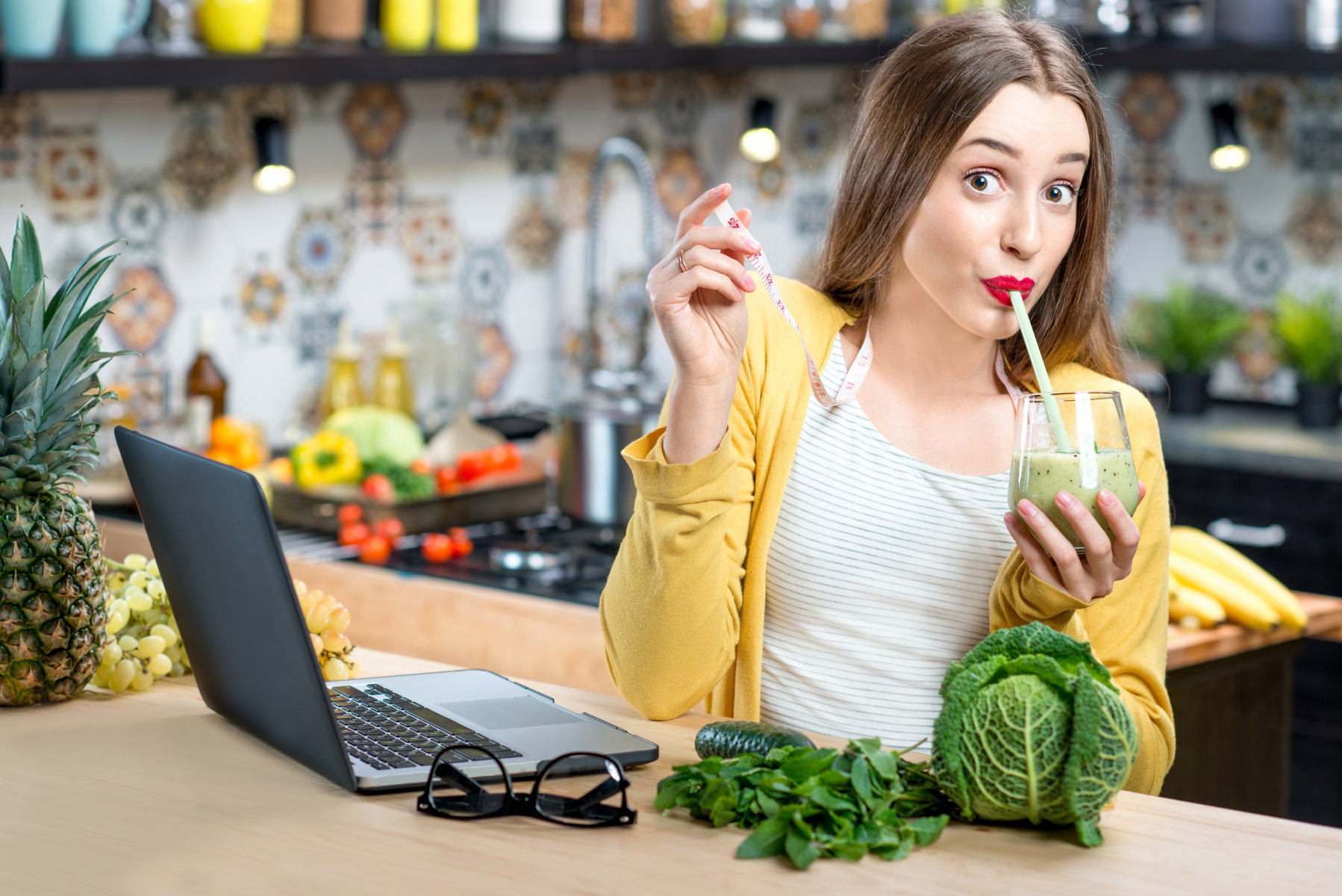 Kobieta siedząca przy blacie w kuchni, pijąca zielone smoothie.