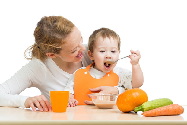 baby eating vegetables puree by spoon himself and sitting on mother laps