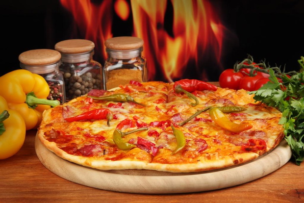 Tasty pepperoni pizza with vegetables on wooden board on flame background