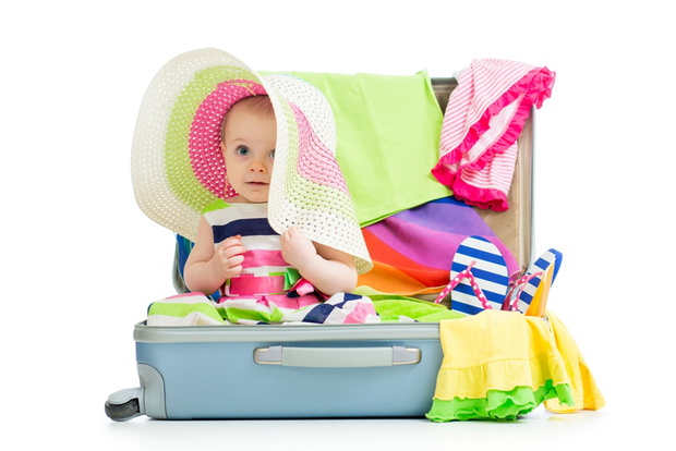 Baby girl sitting in suitcase with  things for vacation travel