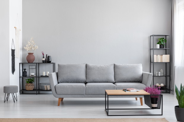Flowers in wooden table in front of grey settee in modern simple apartment interior with stool. Real photo