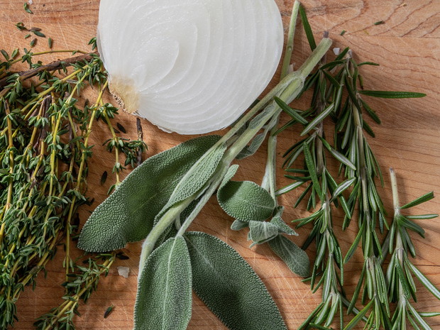 Assortment of spices chicken including garlic, onion, thyme, sage and rosemary on a wooden cutting board.