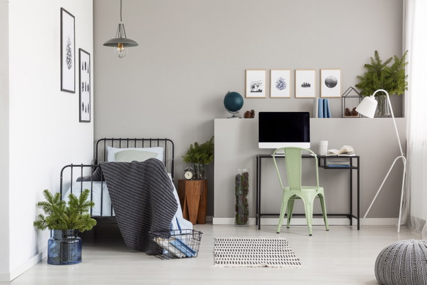 Bright grey bedroom interior with workspace with desk and computer, real photo with copy space on the empty wall
