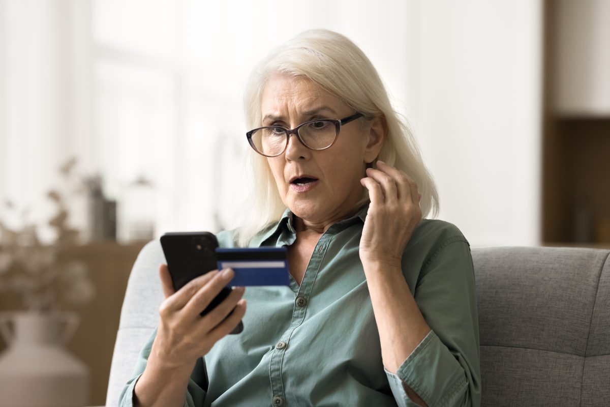 Worried surprised elderly woman in glasses looking at smartphone