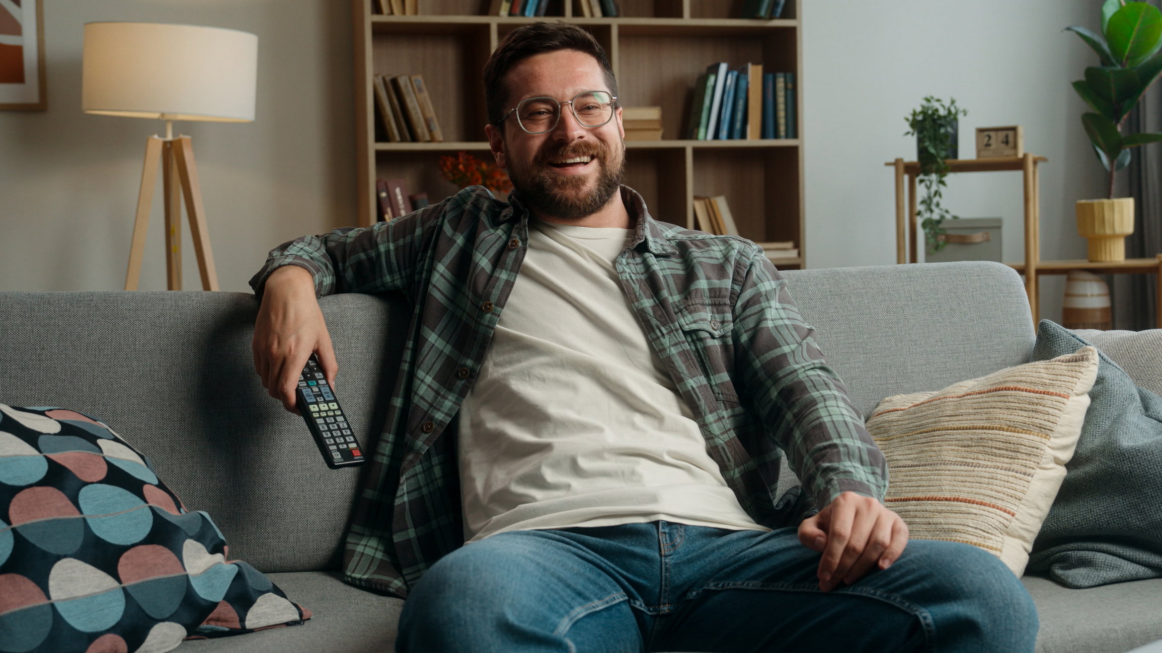 Smiling happy carefree Caucasian man male guy at home couch sofa indoors holiday weekend resting relaxing switch channels with remote control watching TV watch television program film movie sport game