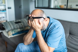Mature adult man with depression sitting on sofa at home