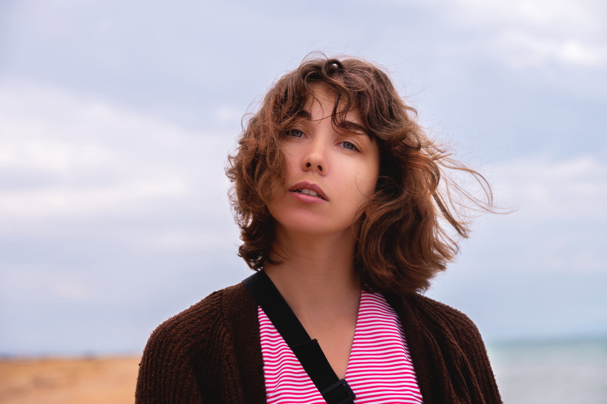 Portrait of a pensive young Caucasian woman with a short haircut. The wind caresses her hair against the backdrop of the beach and sea in cloudy rainy weather