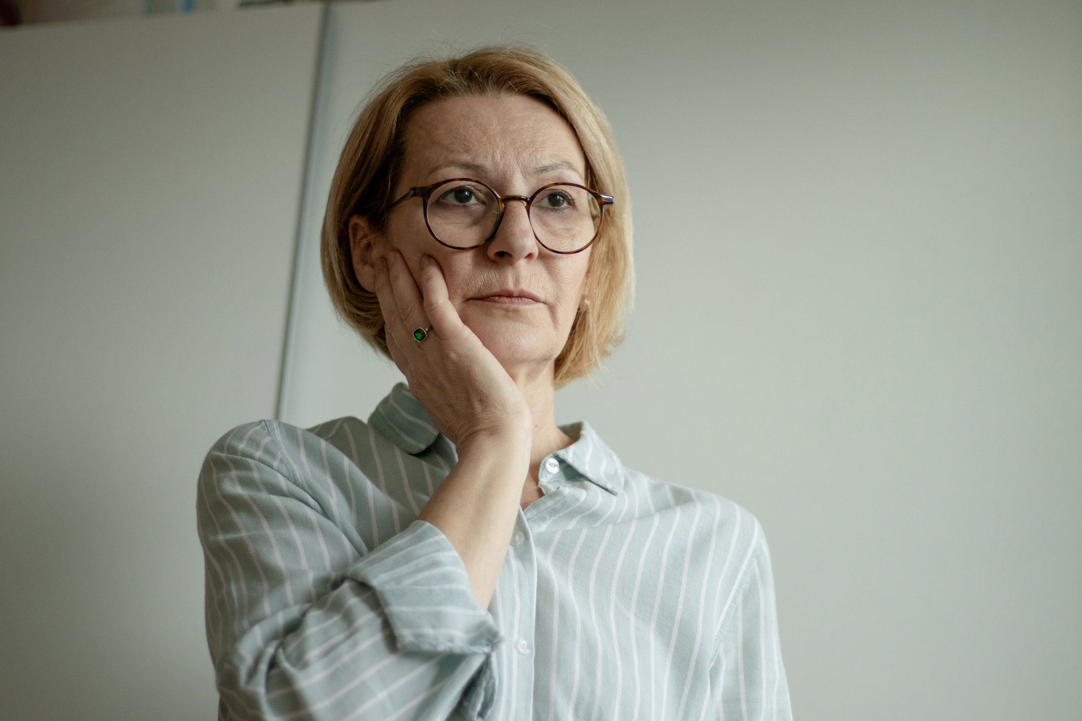 mature blond woman with glasses is alone and stands in the room pensive and depressed