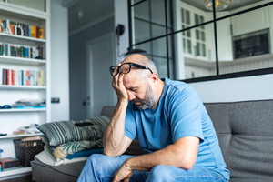 Mature adult man with depression sitting on sofa at home