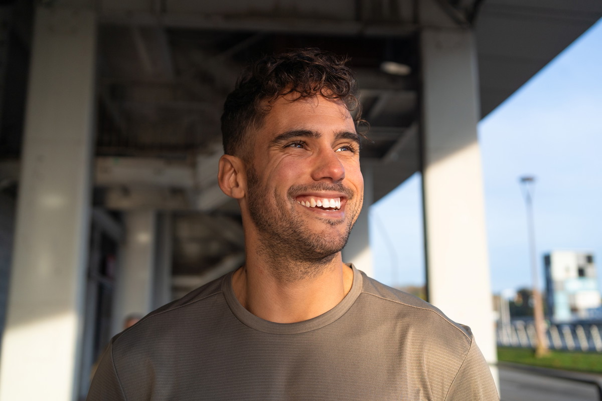 Confident athlete smiles while standing beneath a bridge in an urban environment