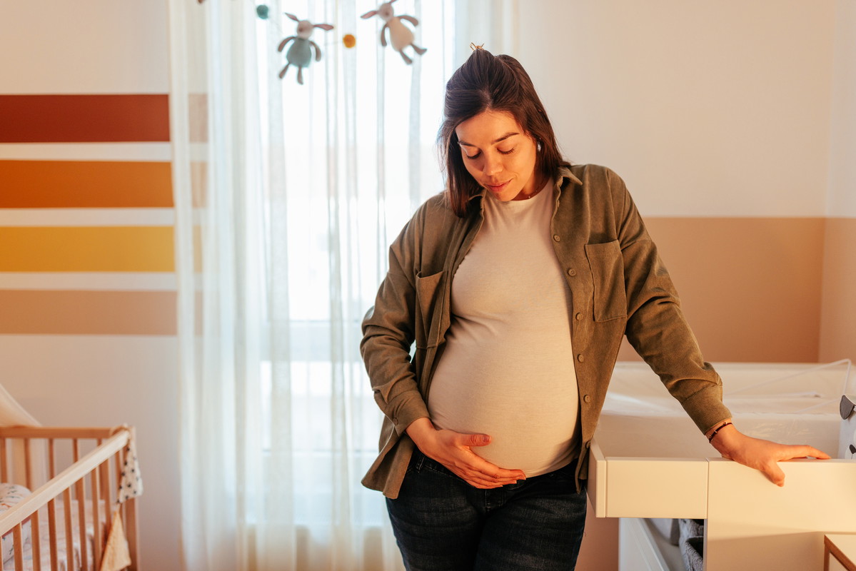Pregnant woman holding stomach at home.