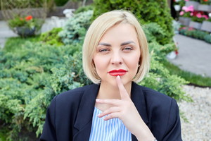 młoda kobieta blondynka z ustami pomalowanymi na czerwono siedzi na zewnątrz zamyślona