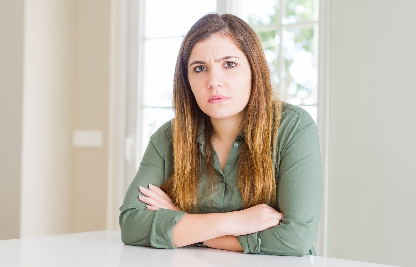 Beautiful young woman at home skeptic and nervous, disapproving expression on face with crossed arms. Negative person.