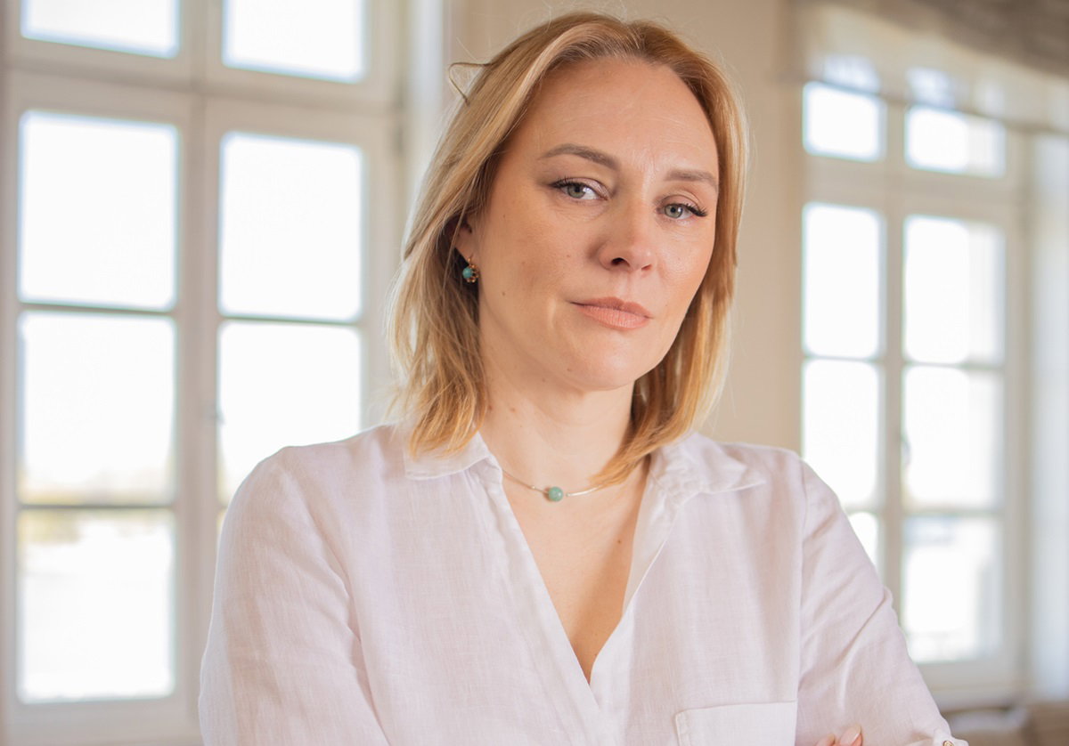 kobieta w średnim wieku blondynka w białej koszuli stoi na tle okna i patrzy powątpiewająco