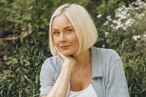 kobieta w wieku około 40 lat blondynka siedzi na tle zieleni i patrzy podejrzliwie