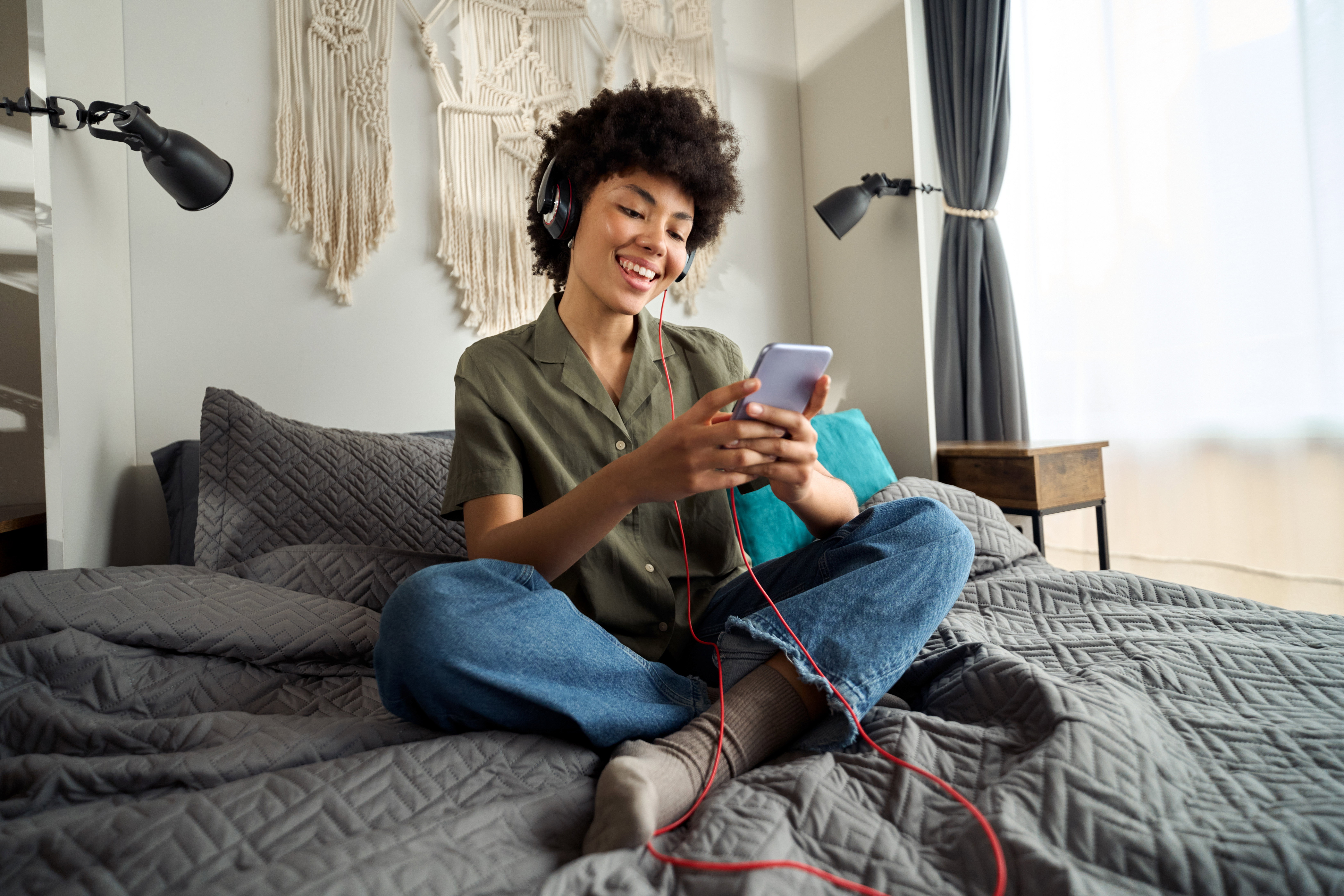 Young happy funky African woman wearing headphones using phone at home.