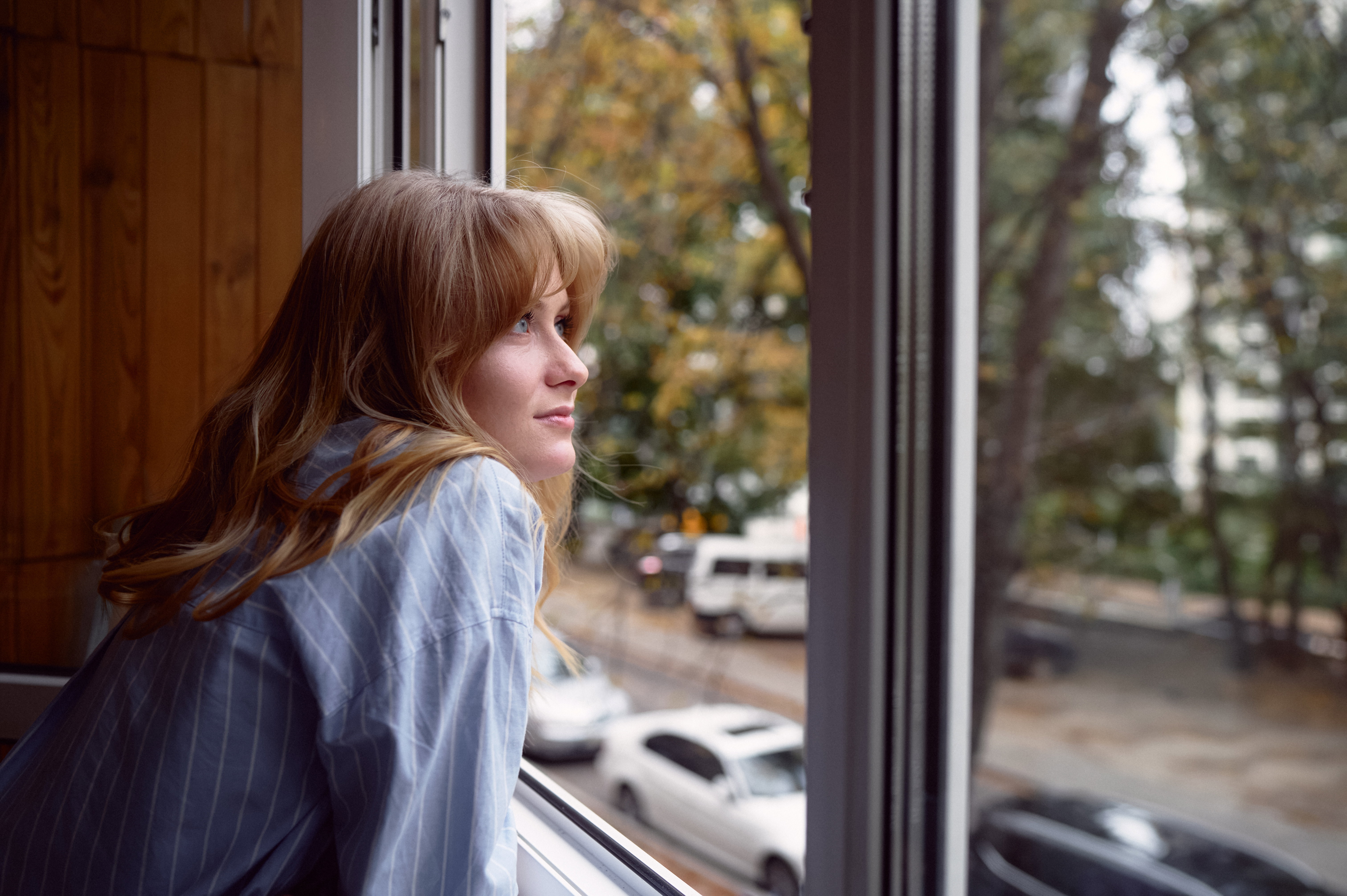 Woman Gazing Out Window During Autumn Day in Urban Neighborhood