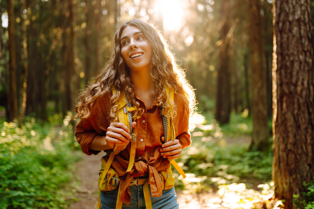 A happy young woman with curly hair walks along a forest path.