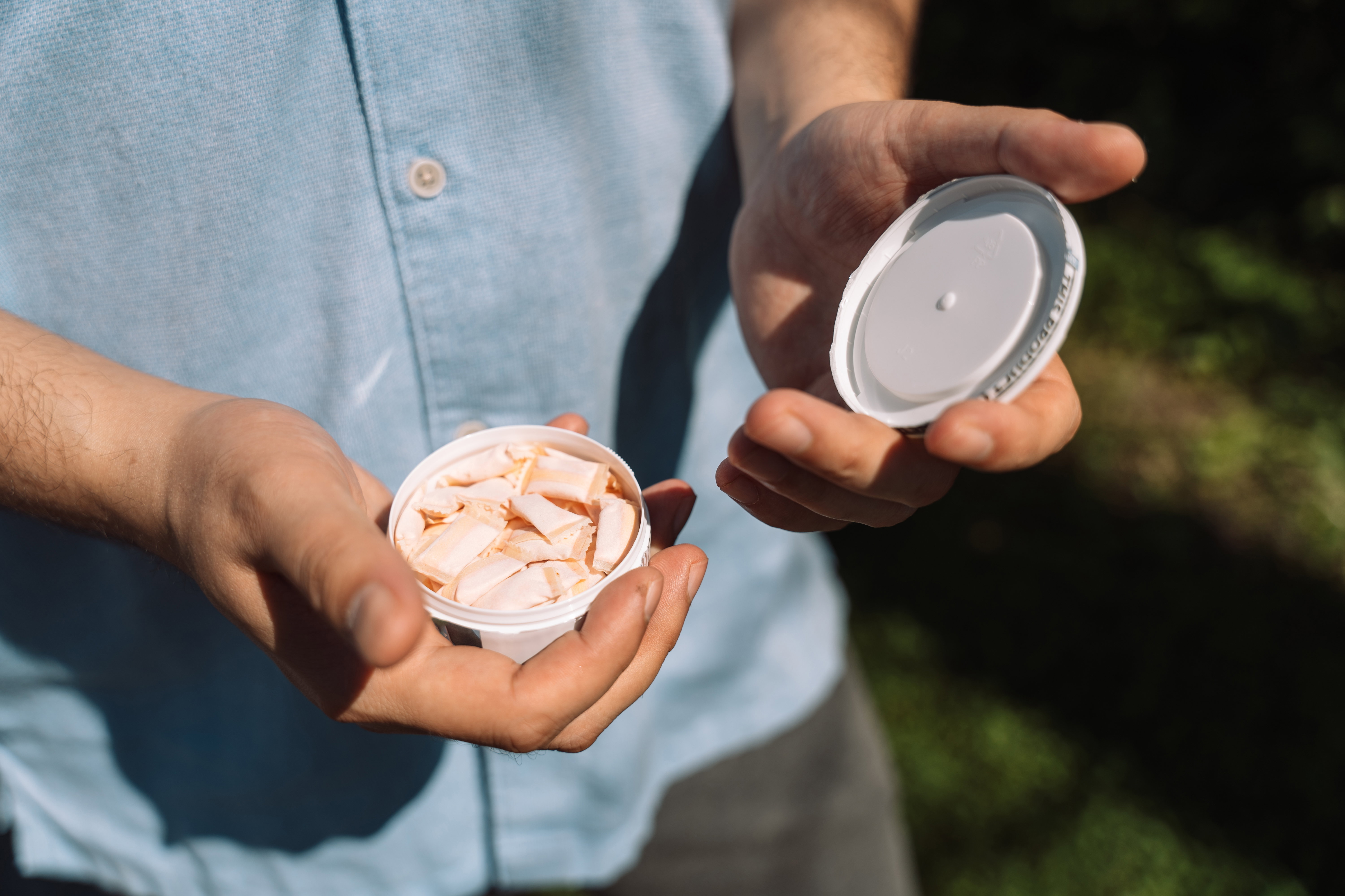 A man opens a plastic can of snus
