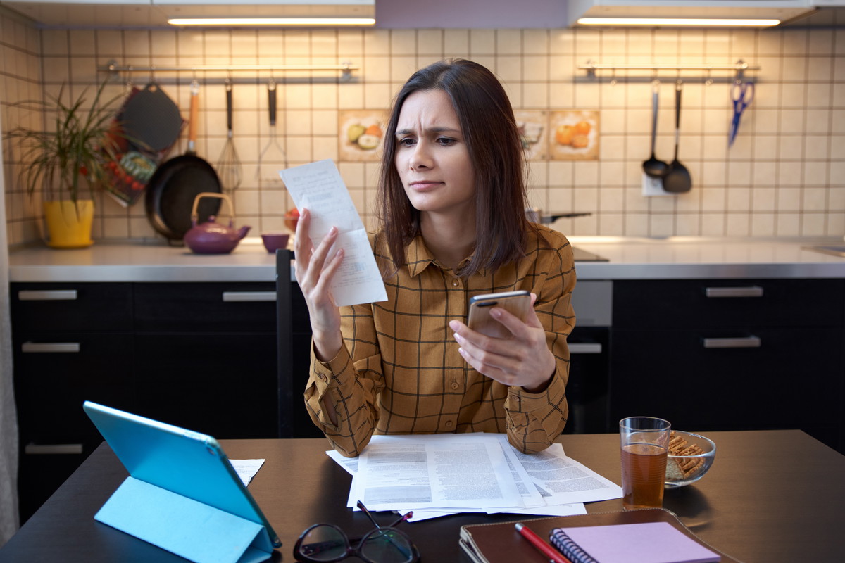 An attractive young housewife wears a shirt at home and examines gas and electricity bills. grimly considers spending this month and is under stress when checking accounts.