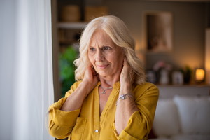 Senior woman suffering neck pain at home: touching sore neck