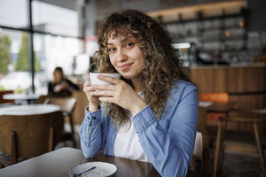 Portrait of young smiling woman drinking coffee in a cafe