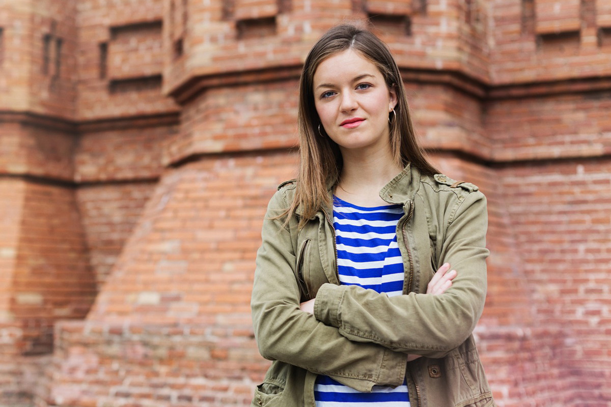młoda dziewczyna w wieku 18 plus w zielonej kurtce stoi na tle murów poważna i zadziorna