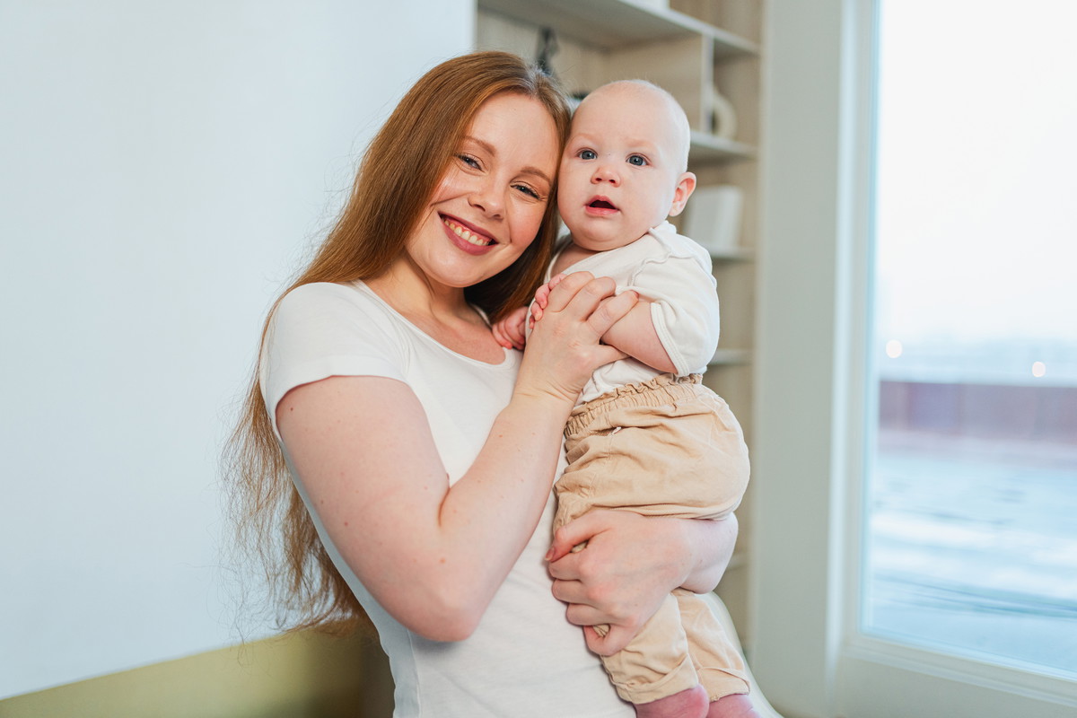 Happy family at home. Mother holding little toddler child daughter. Mom and baby girl relax playing having fun together at home. Mother hugs baby with love care. Mom of breast feeding baby.