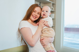 Happy family at home. Mother holding little toddler child daughter. Mom and baby girl relax playing having fun together at home. Mother hugs baby with love care. Mom of breast feeding baby.