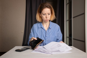 Woman with an empty wallet and utility bills, financial struggle and expense management, debt and payment crisis