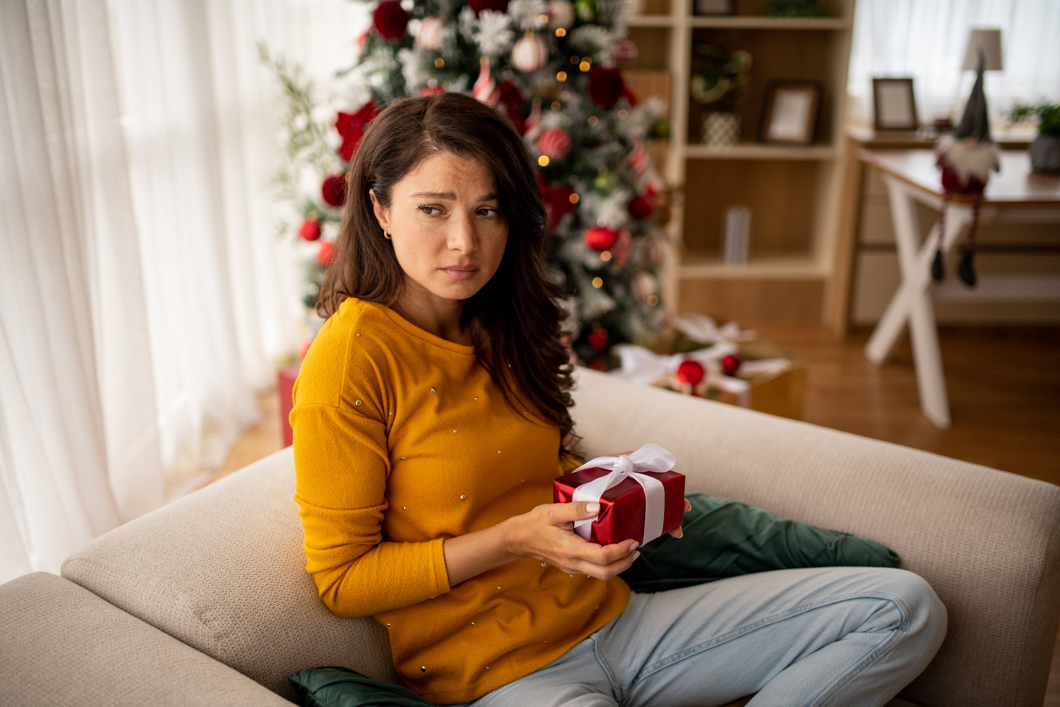 Worried woman with Christmas gift on sofa