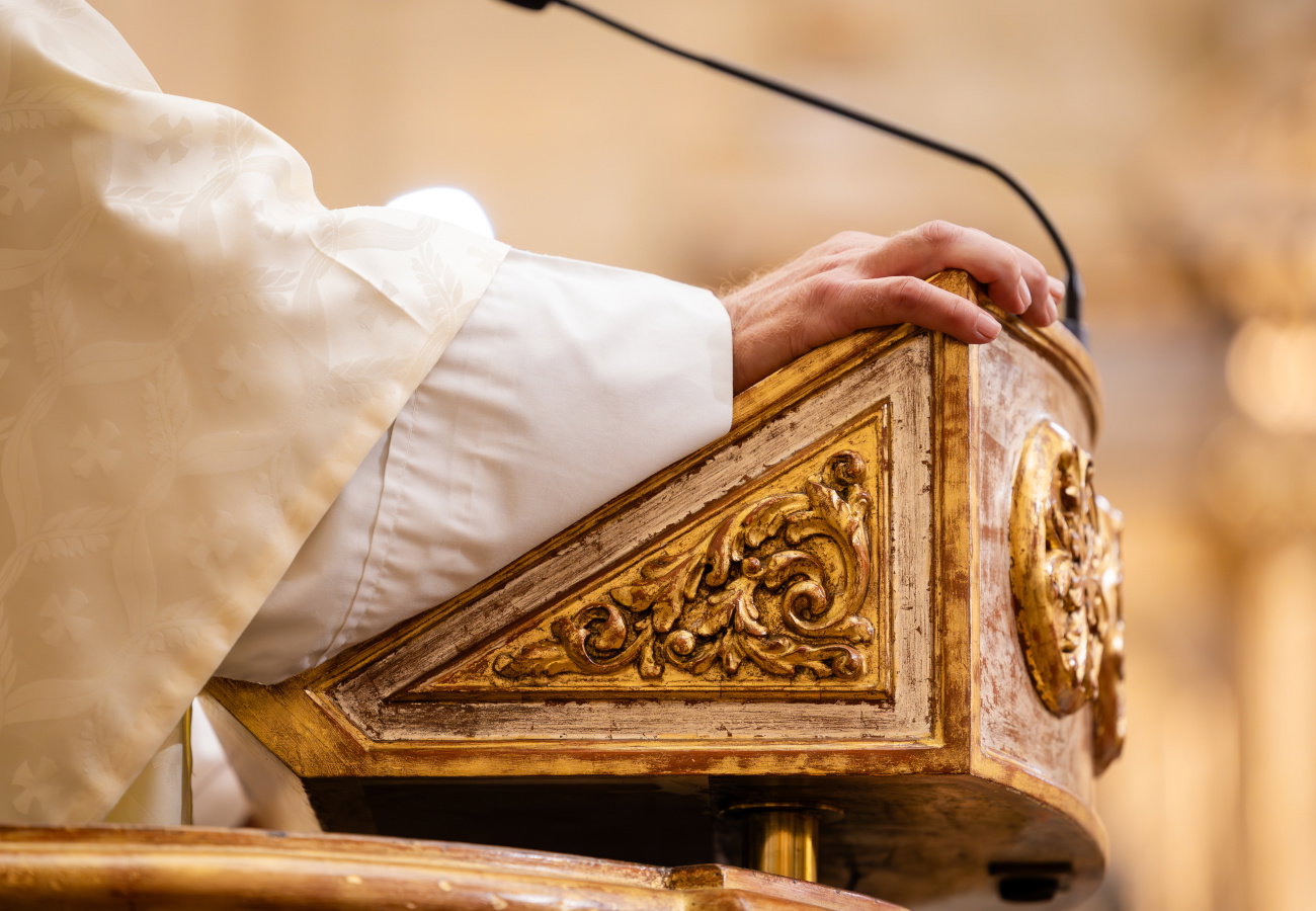 Priest's hand resting on ornate church pulpit during ceremony
