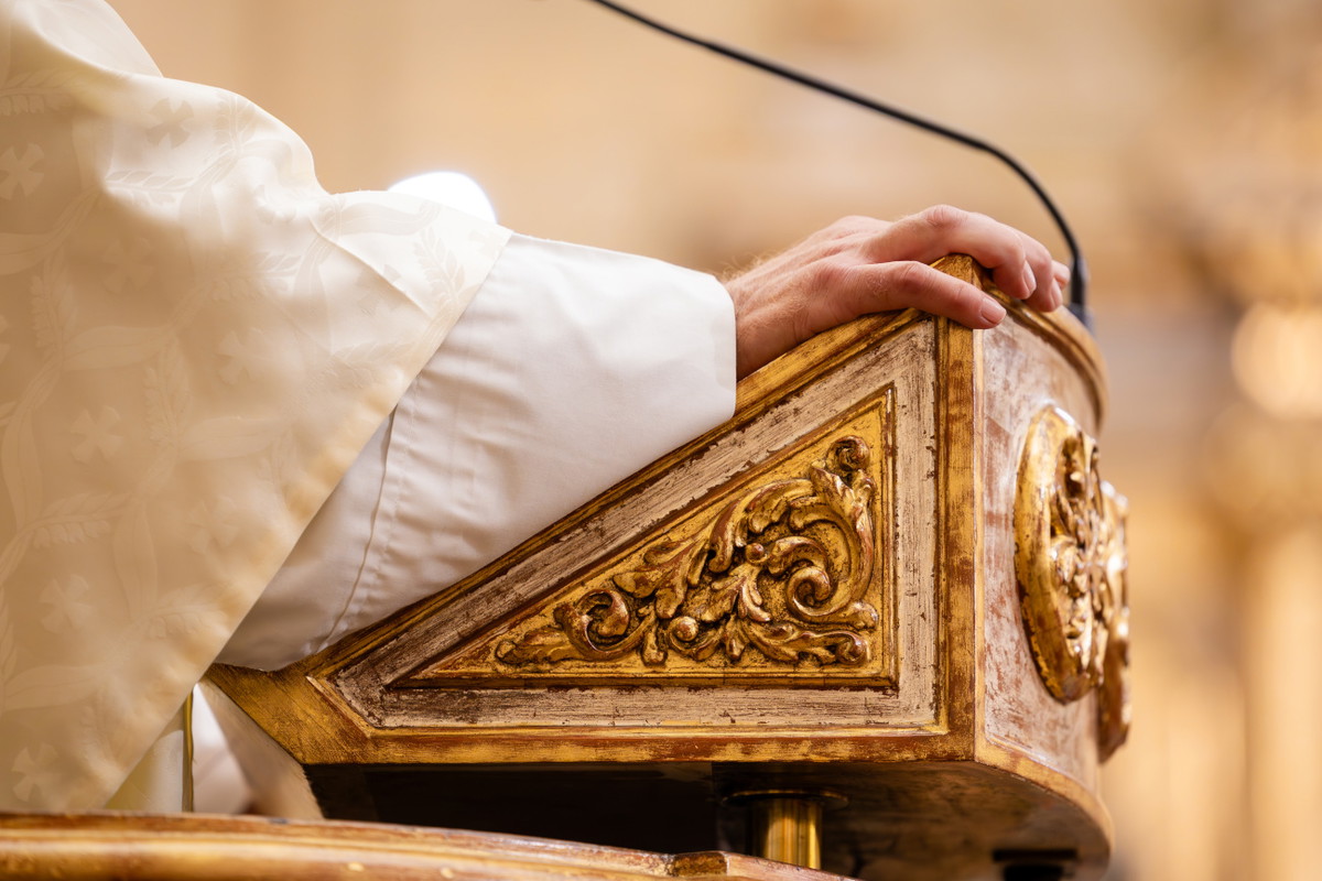 Priest's hand resting on ornate church pulpit during ceremony