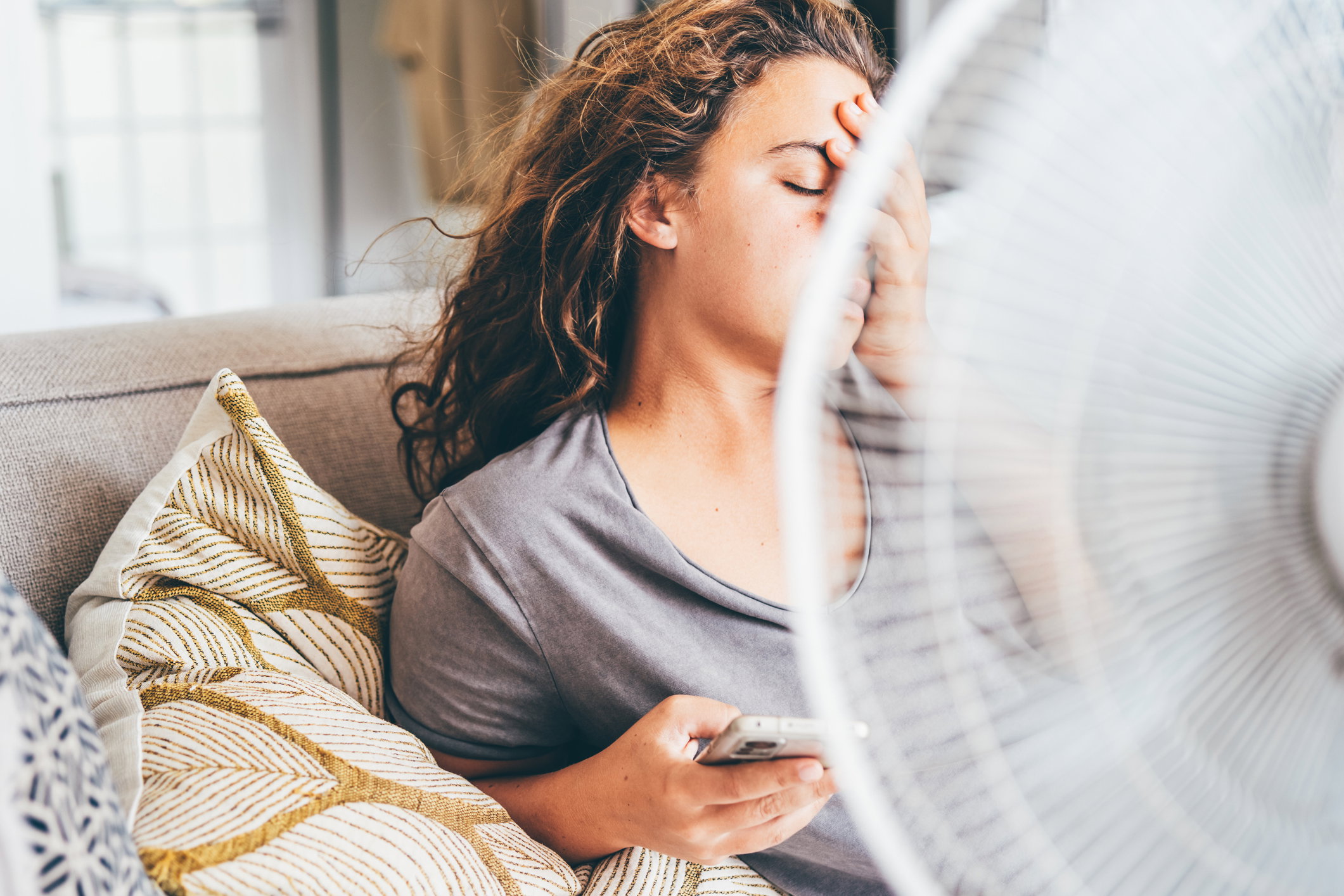 Happy contented woman using electric fan at home enjoying fresh air on hot summer day.