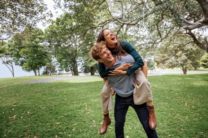 Cheerful young man giving piggyback ride to his girlfriend outdoors at the public park